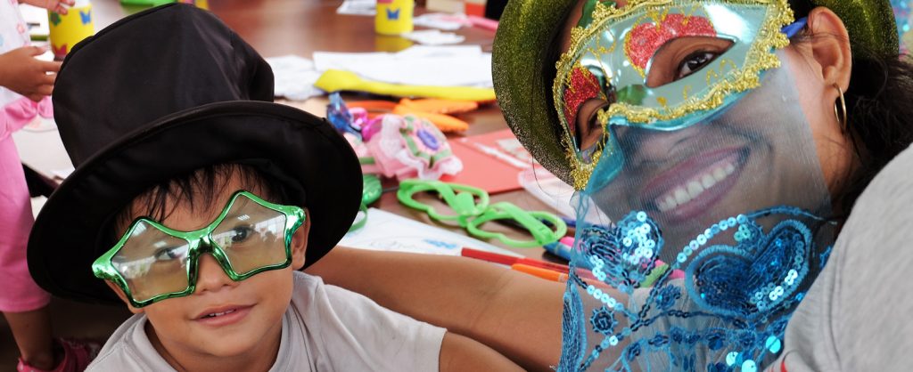 Madre e hijo usando máscaras y gafas decorativas. Detrás se ven los materiales de varias manualidades.